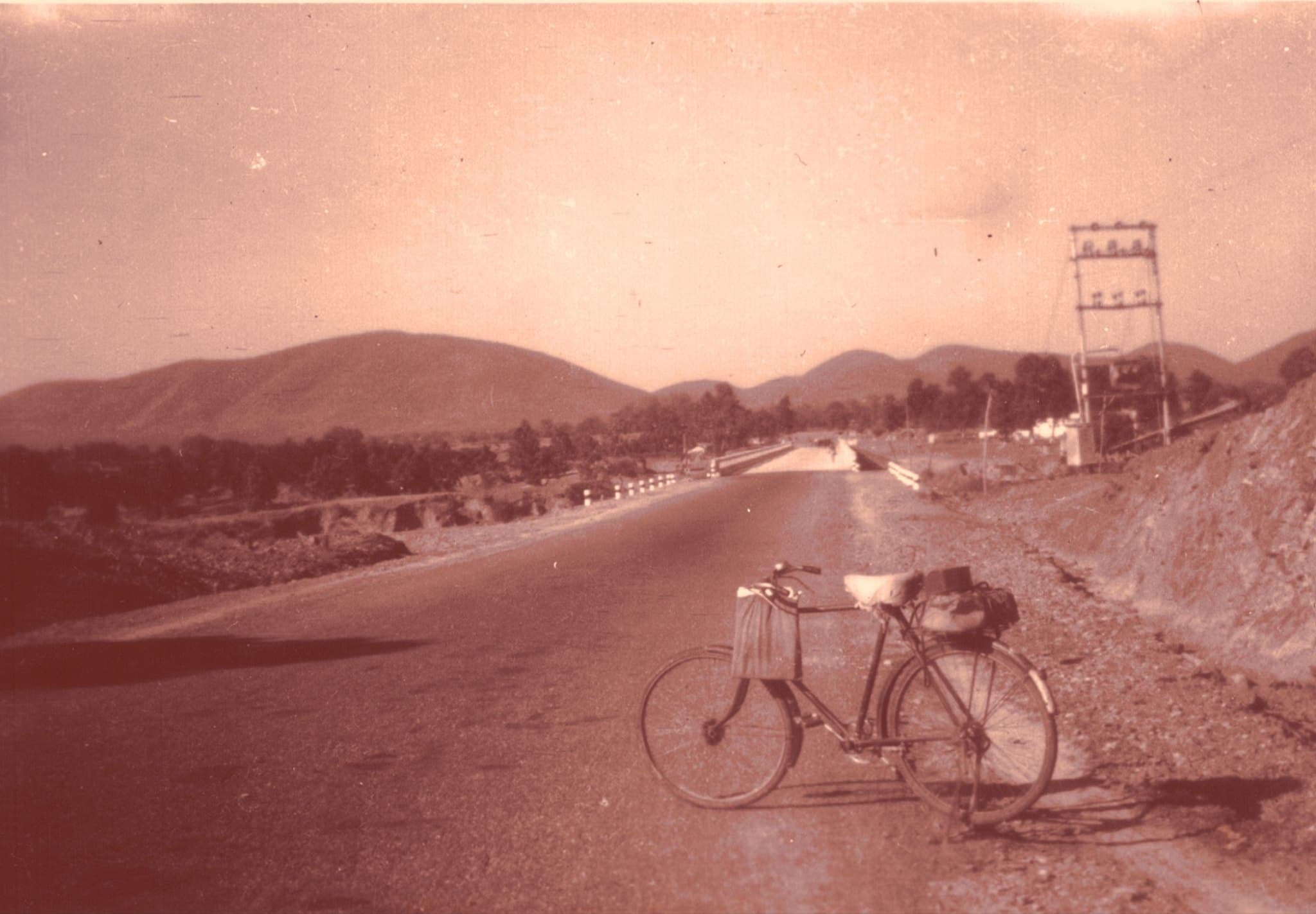 An archive photograph of an empty road running towards low hills, with a bicycle resting at the roadside.
