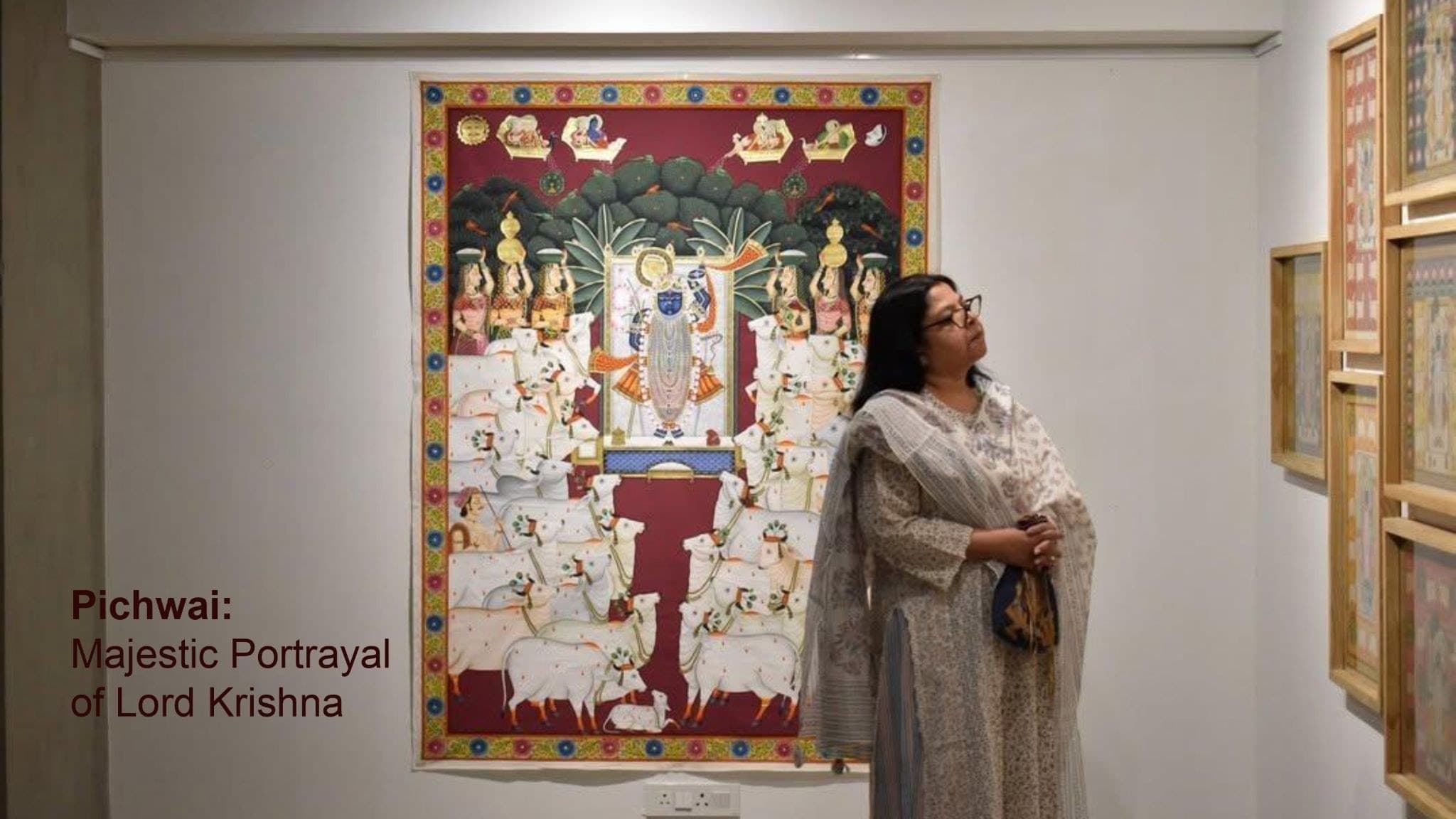 A visitor looking up at a large red-bordered Pichwai painting.