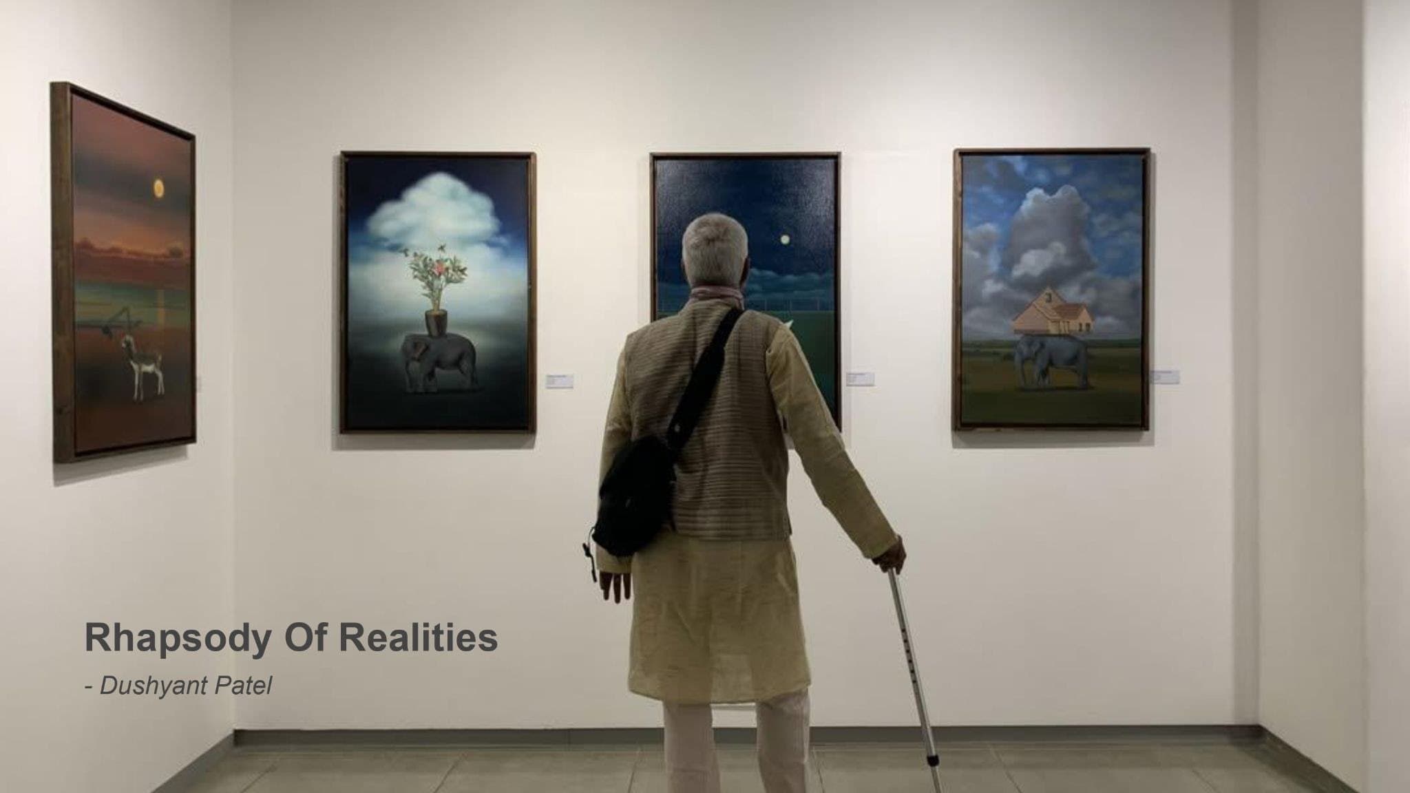 A visitor with a walking stick standing before three paintings.