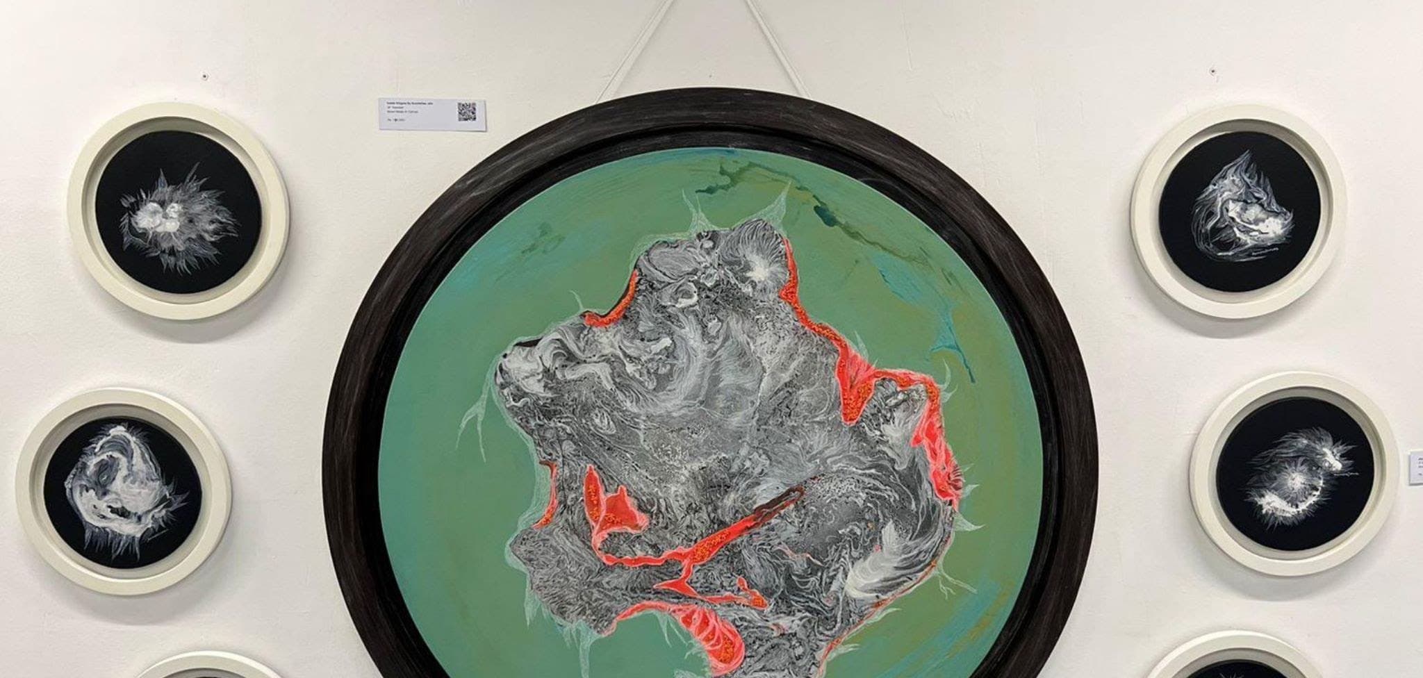 A large circular painting in green, grey and orange, surrounded by six smaller round works in white frames.